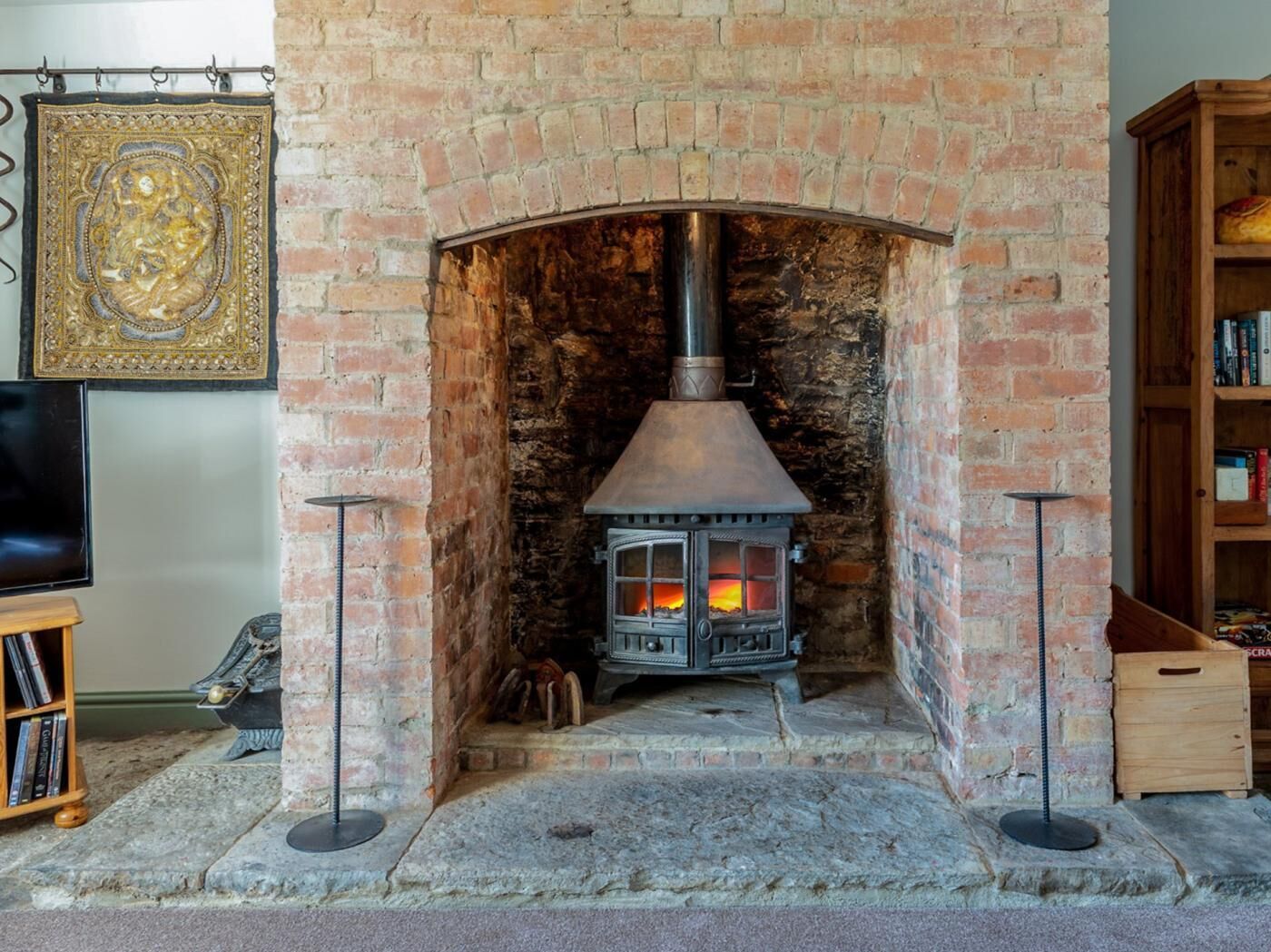 A brick fireplace with a wood-burning stove, a decorative wall piece, and a bookshelf.