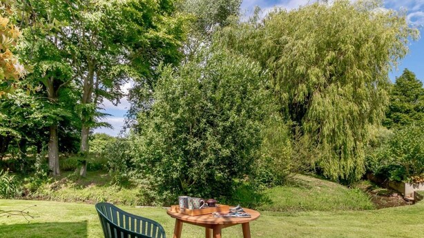 Un espace extérieur aménagé avec deux chaises et une table, entouré d’une végétation luxuriante et d’arbres.