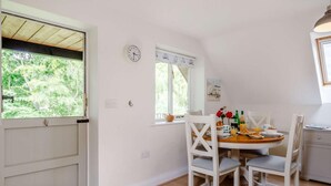 Un coin repas avec une table ronde, des chaises blanches, une horloge au mur et une fenêtre avec des rideaux.
