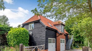 Une maison en bois à deux étages, avec un toit recouvert de tuiles rouges, une allée en gravier et un portail en bois.