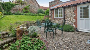A stone building with a red-tiled roof, a garden with a gravel path, and a table with chairs. - 2 Bed in Holt (oc-ncc15) (Salthouse)