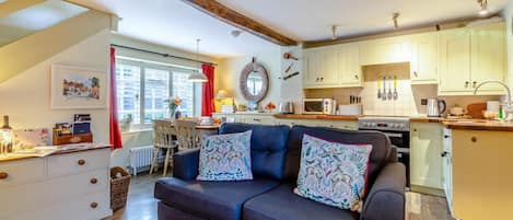 A cozy living room with a dark sofa, a dining area with a table and chairs, and a kitchen with light-colored cabinets and appliances.