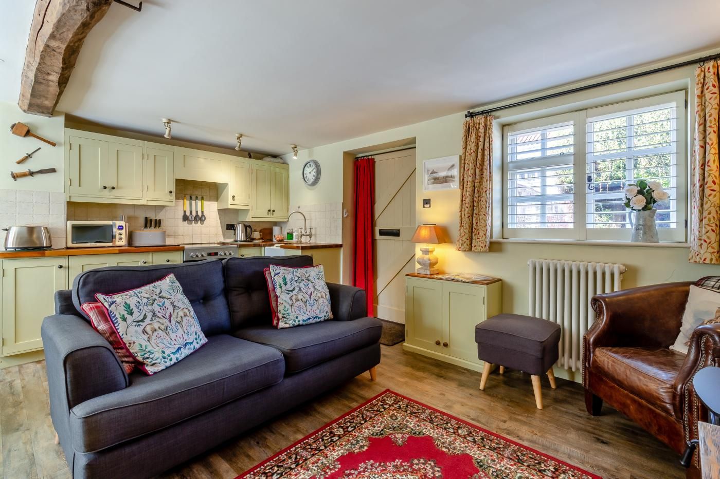 A cozy living room with a sofa, ottoman, and a red patterned rug.