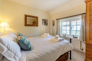 A bedroom with a double bed, a bedside lamp, a window with curtains, and a wooden cabinet. - 2 Bed in Holt (oc-ncc14) (Holt)