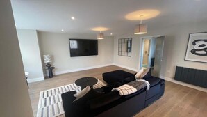 Een moderne woonkamer met een zwarte bank, een ronde salontafel, een flatscreen televisie en een kamerkleed met dessin.