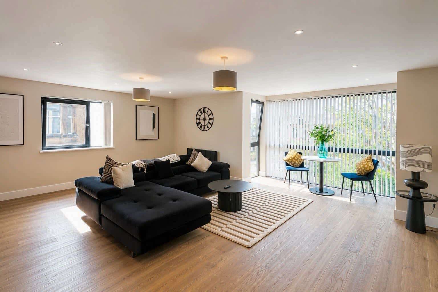 A modern living room with a black sofa, a round coffee table, and a view of the outdoors through large windows.