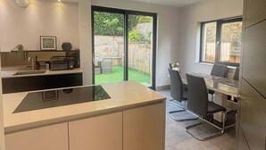 Een moderne keuken met een centraal eiland, een eethoek met een tafel en stoelen, en een uitzicht op een tuin door grote schuifdeuren.