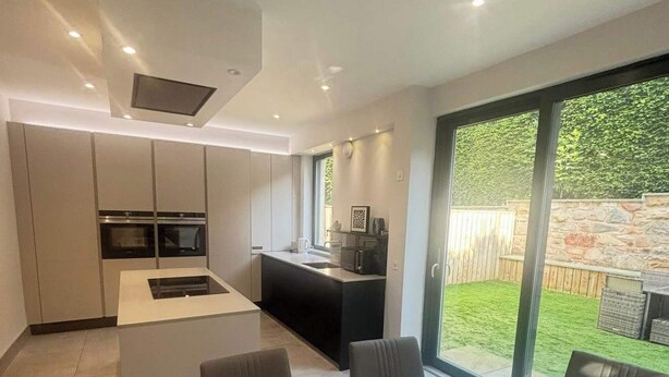 Een moderne keuken met inbouwapparatuur, een eethoek met een glazen tafel en een grote schuifpui naar een achtertuin.