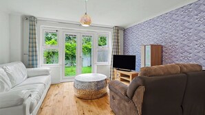 Een woonkamer met een witte bank, een bruine bank, een ronde salontafel en een televisie op een houten dressoir.