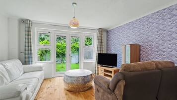 A living room with a white sofa, a brown sofa, a round coffee table, and a television on a wooden stand.