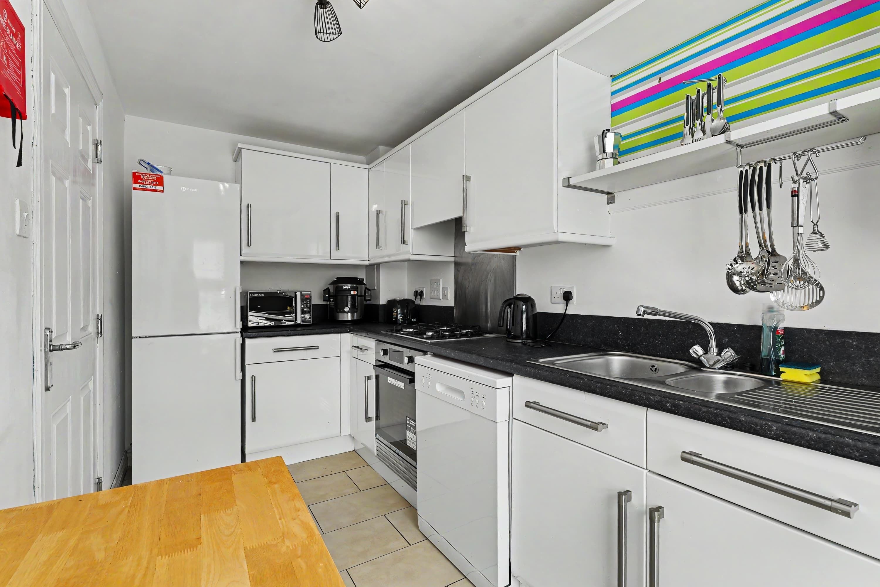 A modern kitchen with white cabinets, a black countertop, stainless steel appliances, and a colorful striped backsplash.