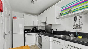 Een moderne keuken met witte kasten, een zwart aanrecht, roestvrijstalen apparatuur en een kleurrijke, gestreepte spatwand.