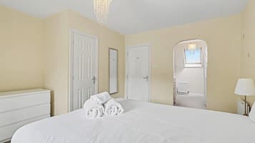 A hotel room with a large bed, white walls, and a chandelier.