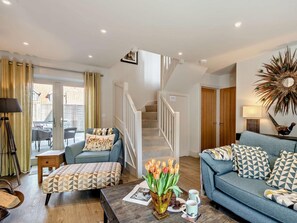 Ein Wohnzimmer mit einer Couch, einem Hocker und einem Couchtisch mit Blumen.