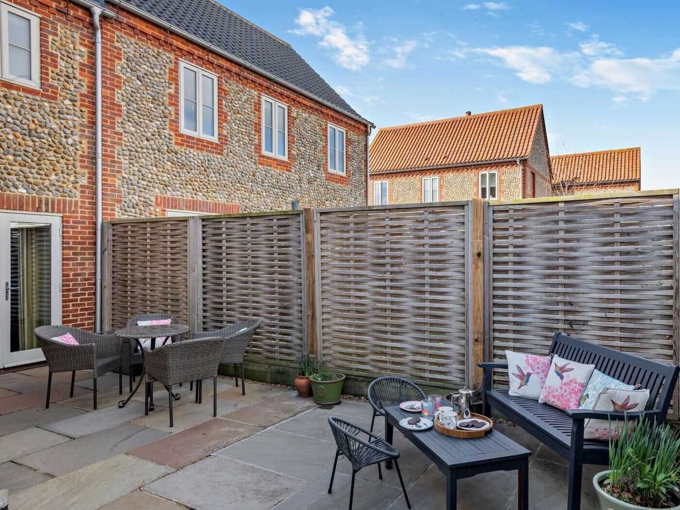 Une terrasse avec des meubles en osier, une table sur laquelle se trouve un plateau de nourriture et une clôture en bois.