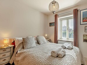 Ein ordentlich bezogenes Bett mit einer gemusterten Decke, einer Nachttischlampe und einem Fenster mit Vorhängen.