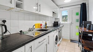 A modern kitchen with white cabinets, a built-in washing machine, and a coffee machine. - Charming 1-Bedroom Hideaway in Central Falkirk (Falkirk)