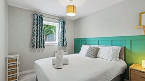 A bedroom with a bed, a nightstand, a window with curtains, a wall-mounted shelf, and a ceiling light. - Charming 1-Bedroom Hideaway in Central Falkirk (Falkirk)
