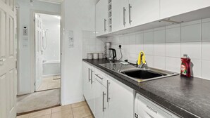 A modern kitchen with white cabinets, a black countertop, a sink, and a coffee maker. - Charming 1-Bedroom Hideaway in Central Falkirk (Falkirk)