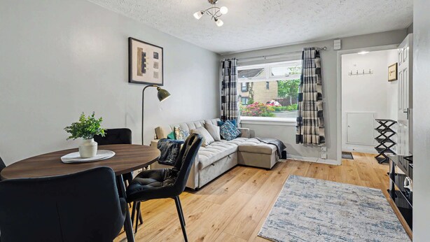 A modern living room with a sofa, a dining table with chairs, a ceiling light fixture, and a window with curtains. - Charming 1-Bedroom Hideaway in Central Falkirk (Falkirk)