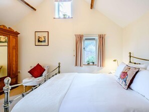 Ein Schlafzimmer mit einem Bett, einem Fenster mit Vorhängen, einem Holzschrank und einem gerahmten Bild an der Wand.