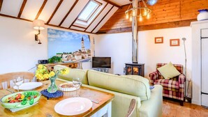 Quarto aconchegante com uma mesa de jantar, sofá e televisão. Teto de madeira e uma janela grande.