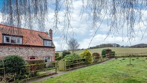 A stone house with a red-tiled roof, a wooden fence, and a grassy field in the background. - 2 Bed in Holt (oc-ncc25) (Kelling)
