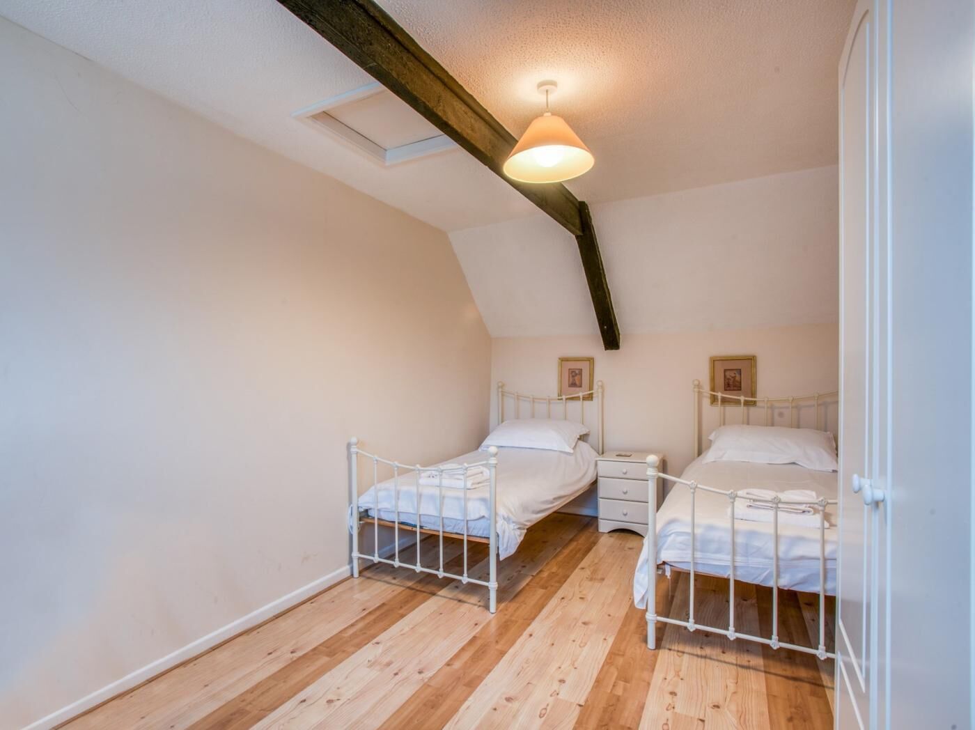 Une chambre avec deux lits, un plancher en bois, des murs blancs et un plafond en pente avec des poutres apparentes.
