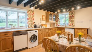 A kitchen with wooden cabinets, a washing machine, a dining table set with chairs, and a view of the outdoors. - 2 Bed in Holt (oc-ncc25) (Kelling)