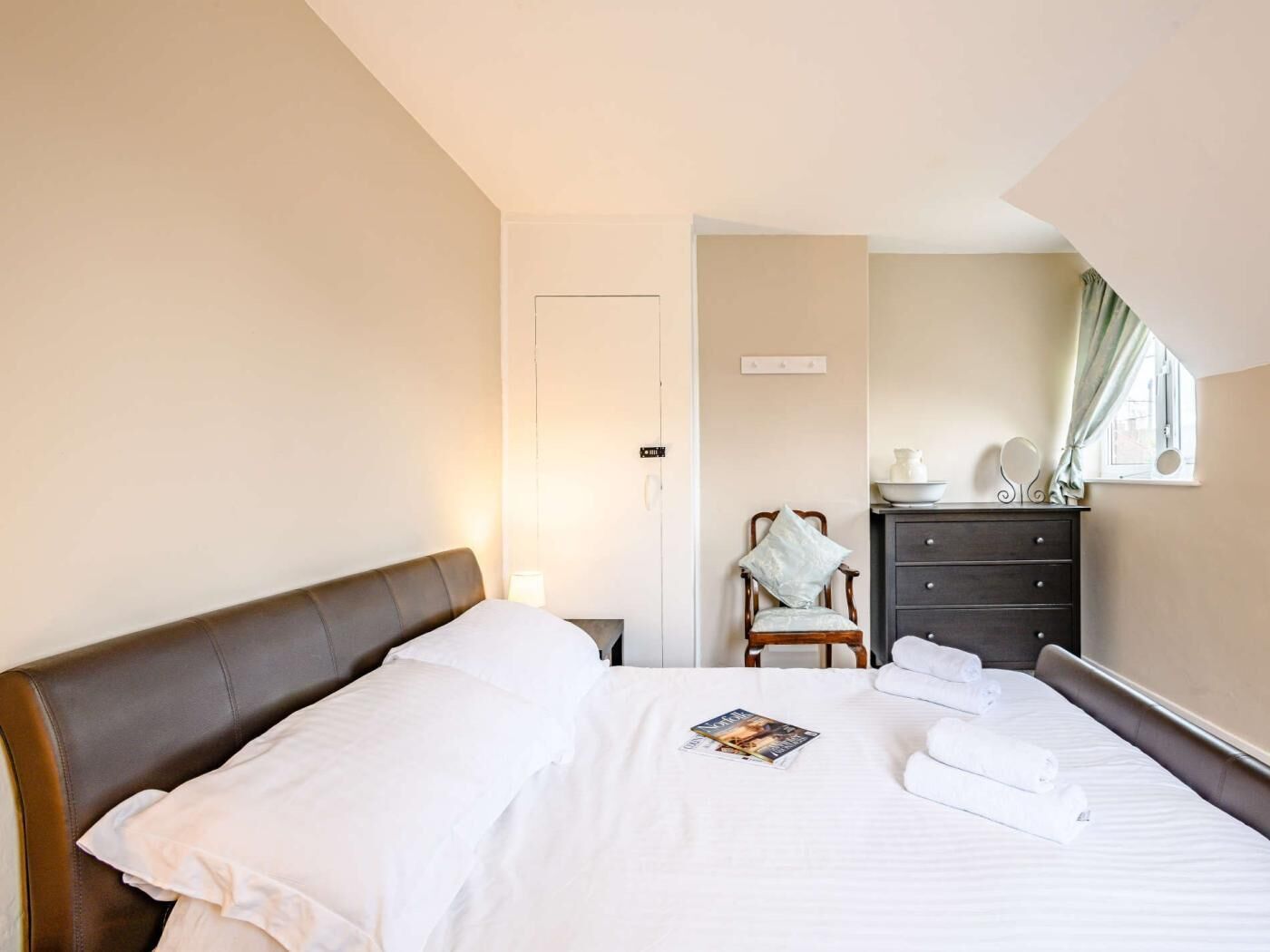 A hotel room with a bed, a chair, a dresser, and a window with curtains.