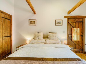 A bedroom with a large bed, wooden beams on the ceiling, two bedside tables with lamps, and a wooden wardrobe. - 2 Bed in Brampton (oc-73578) (Low Row)