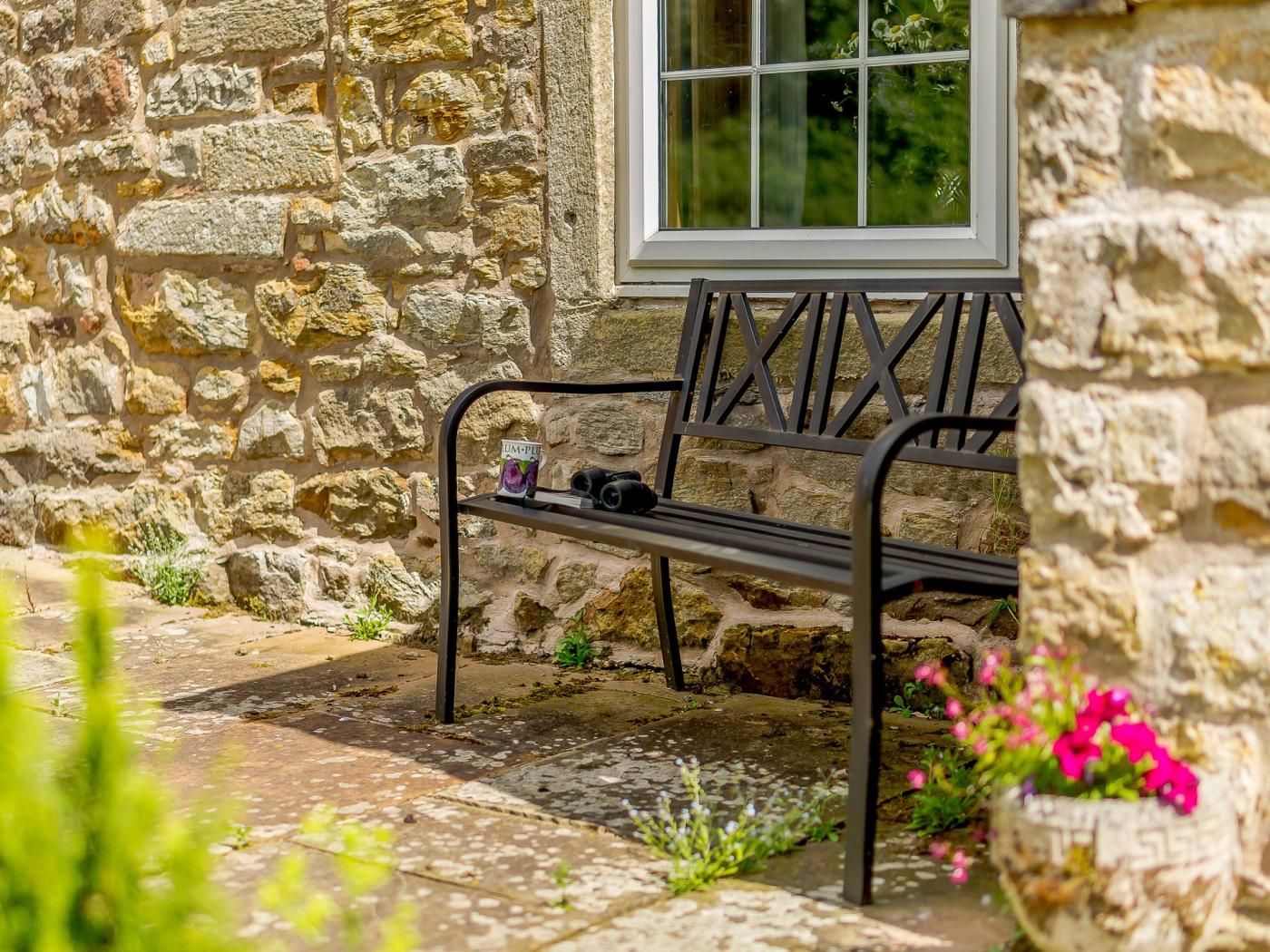 A stone building with a window, a bench with a sign, and a flower pot.