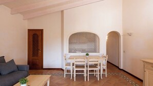 A living room with a sofa, a coffee table with a plant, a dining table with chairs, and a door with a lattice design. - Casa Tozzi by Wonderful Italy (Arzachena)