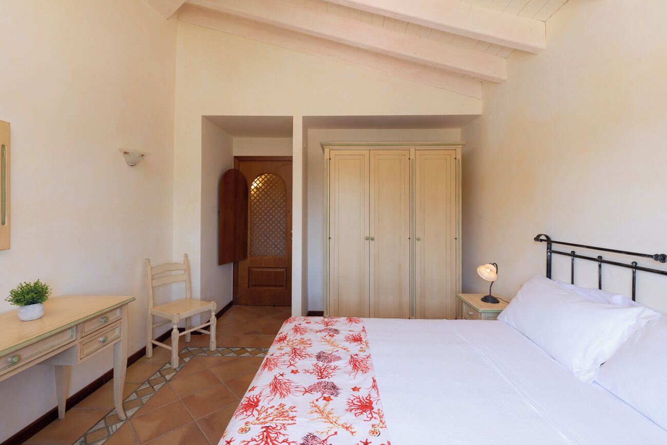 Une chambre à coucher comprenant un lit, un bureau avec une chaise, une armoire et une table de chevet avec une lampe.