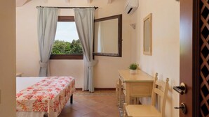 A room with a bed, a desk, a chair, a window with curtains, a mirror, and a potted plant. - Casa Tozzi by Wonderful Italy (Arzachena)