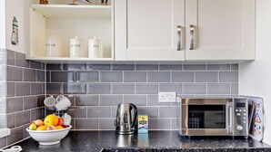 A kitchen with a microwave, kettle, and a bowl of fruit on the counter. - 2 Bed in Bideford (oc-73433) (Instow)