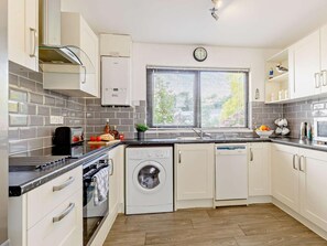 Eine moderne Küche mit integriertem Waschmaschine, einer Uhr und einem Fenster mit Jalousien.
