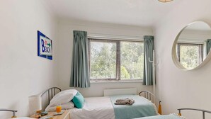 A bedroom with two beds, a bedside table with a lamp, a window with curtains, and a wall-mounted sign. - 2 Bed in Bideford (oc-73433) (Instow)