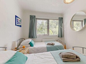Ein Schlafzimmer mit zwei Betten, einem Nachttisch mit Lampe, einem Fenster mit Vorhängen und einem an der Wand befestigten Schild.