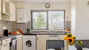 A modern kitchen with a built-in oven, washing machine, and a dining area with a table set for two. - 2 Bed in Bideford (oc-73433) (Instow)