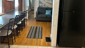 Une cuisine avec un réfrigérateur noir, un coin repas avec des chaises et une table, un canapé gris et un tableau représentant une scène de plage.