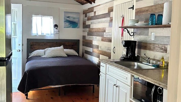 A bedroom with a bed, a nightstand, a desk, and a window.