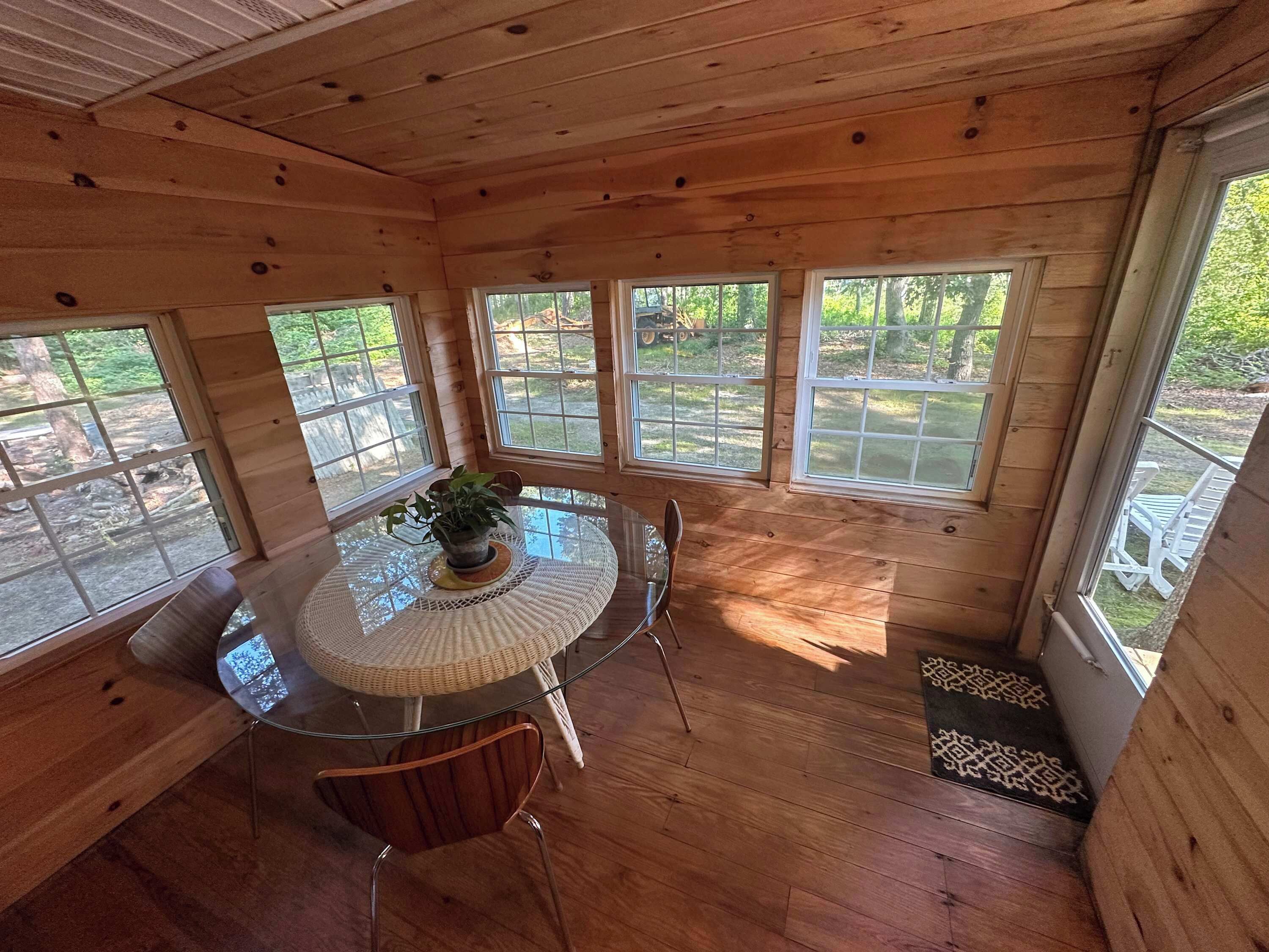 Un intérieur en bois avec une table ronde en verre, des chaises et une plante en pot.