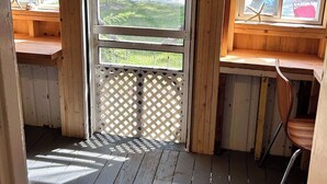 A wooden cabin with a porch, a door leading outside, and a window with a view of a yard.
