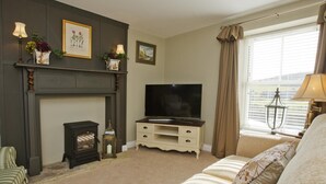 A living room with a fireplace, a television, a sofa, and a window with curtains. - 1 Bed in Pateley Bridge (oc-g0015) (Wilsill)