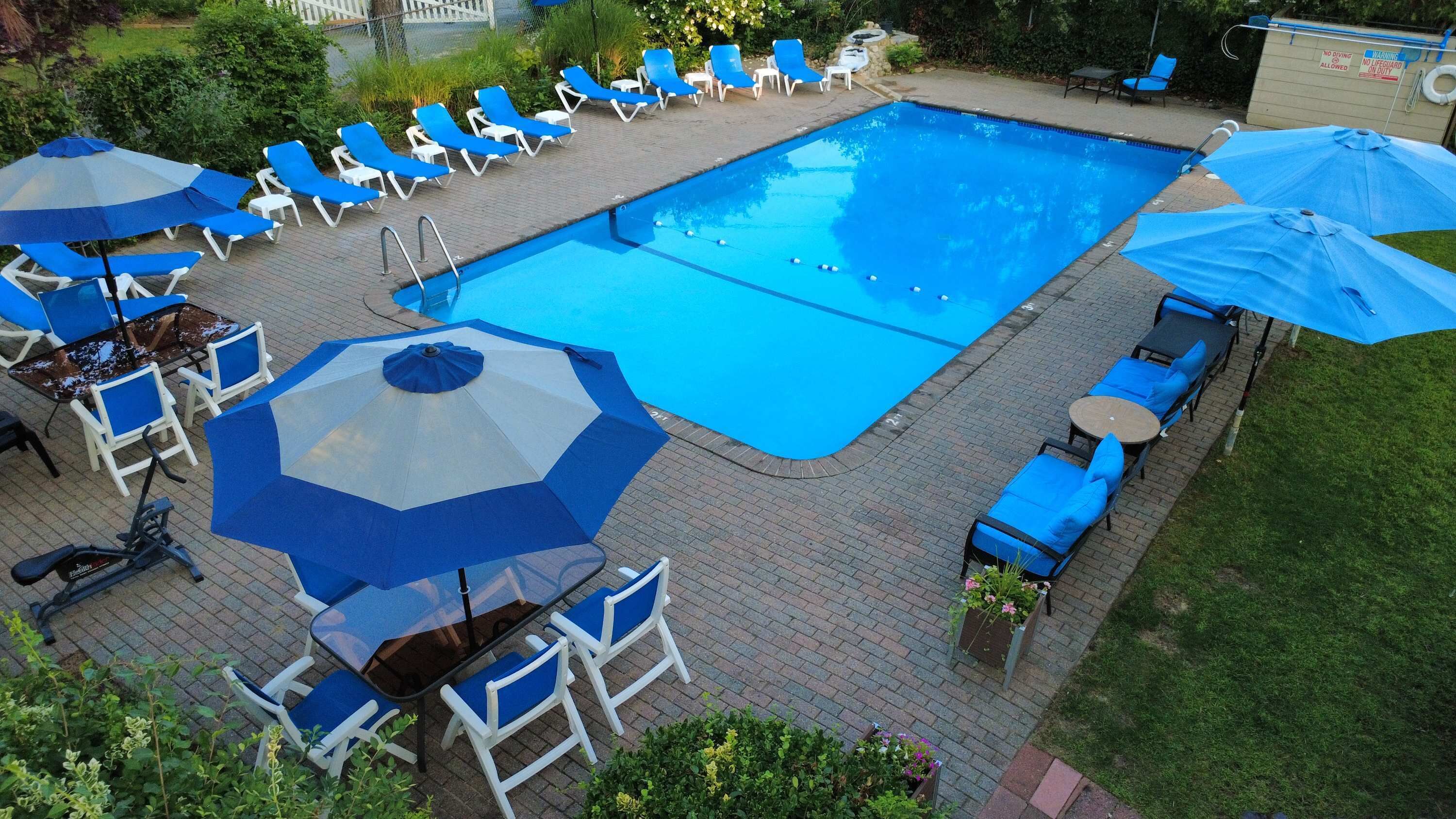 A swimming pool with lounge chairs and umbrellas, surrounded by a brick patio.