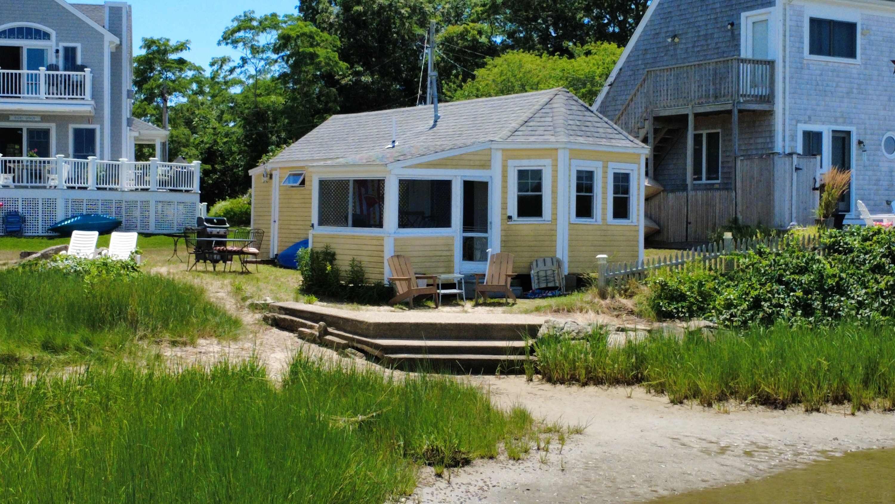 Ein Küstenhaus mit einer kleinen Veranda, zwei Stühlen und einem Grill.