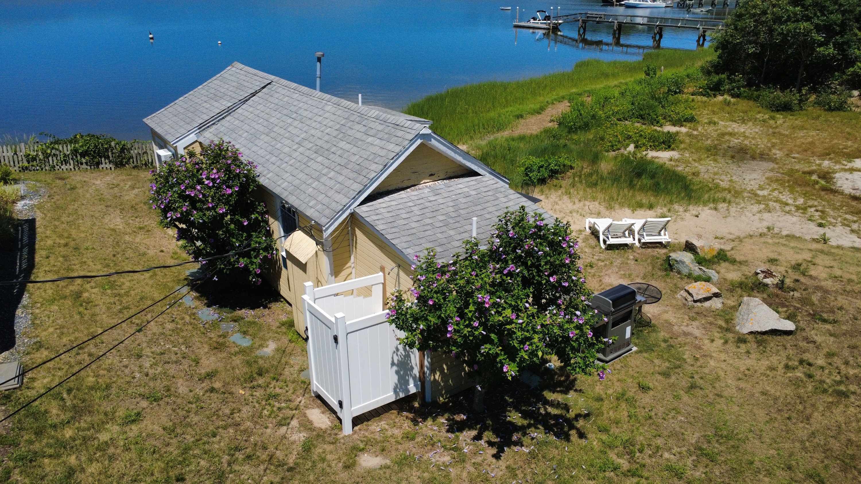 Ein kleines Haus mit Satteldach, einem umzäunten Garten und einem Steg, der sich ins Wasser erstreckt.
