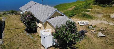 A small house with a sloped roof, a fenced yard, and a dock extending into a body of water.