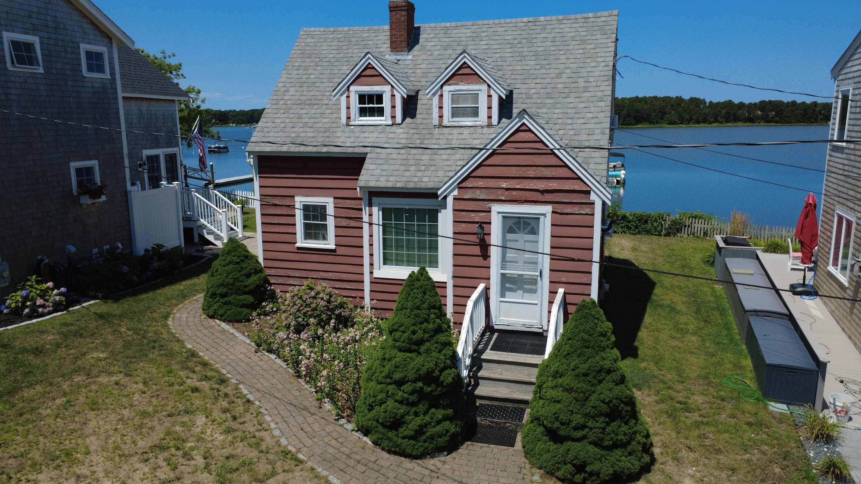 Une maison à deux étages avec un porche à l’avant, une petite terrasse et une vue sur un lac.